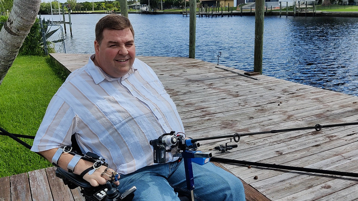 video of executive director Mark  Felling demonstrating Hands-on Adjustable, Hinged Fish Fighting Rod Holder for Wheelchair Seat  on dock in Florida with adaptive fishing electric reel mounted